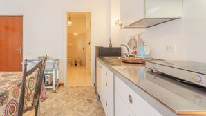 Eine Küche mit einem Edelstahlherd, einer Mikrowelle und einem Spülbecken. Ein Holzbstuhl und ein Tisch mit einem gemusterten Tischläufer sind vorhanden.