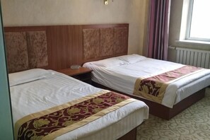 Two single beds with wooden headboards, a bedside table, and a window with curtains. - Sheng'an Hotel (New Barag Left Banner)