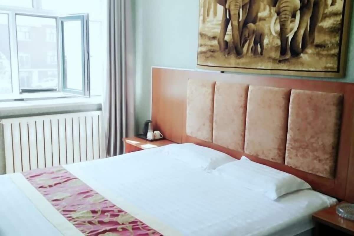 A hotel room with a bed, a headboard, a window, a radiator, and a painting of elephants.