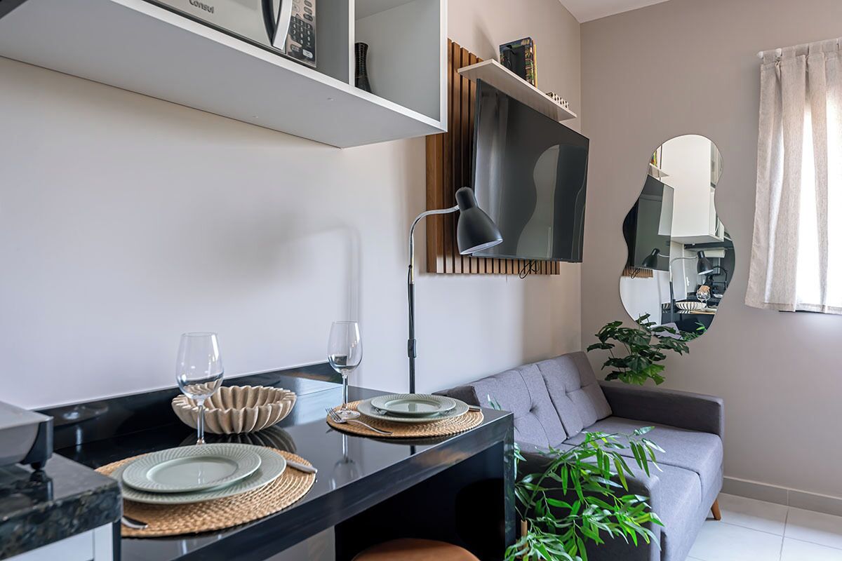 En moderne stue med et spisebord dækket til to personer, en grå sofa, et stort spejl og en potteplante.