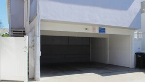 Portão de garagem fechado com o número 121, placa indicando aluguel por temporada, e uma lixeira à direita.
