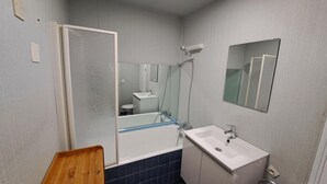 Et badeværelse med badekar, vask, spejl og bruser.