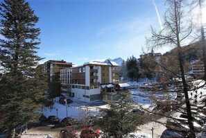 A multi-story building with a snow-covered roof, surrounded by trees and mountains. - 100m from resort center, 9th floor, balcony, parking, tv, ski locker, 32m², Pra Loup (Pra Loup)
