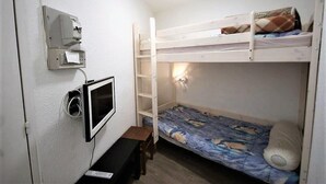 Et soveværelse med køjeseng, skrivebord, vægmonteret TV og stikkontakt.