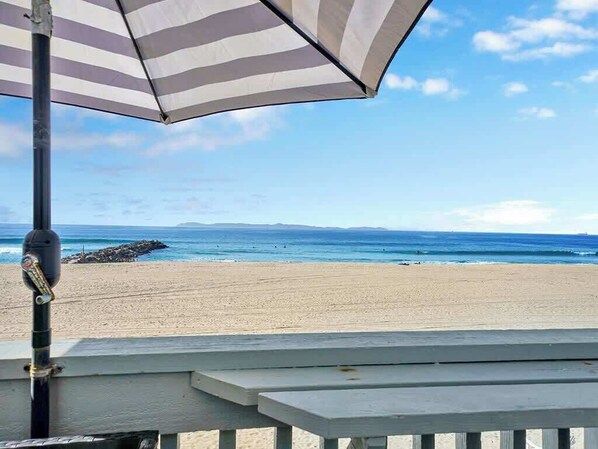A beach view with a striped umbrella and a wooden bench.