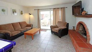 Ein Wohnzimmer mit Sofa, Sessel, Couchtisch, Kamin und Fernseher auf einem Regal.