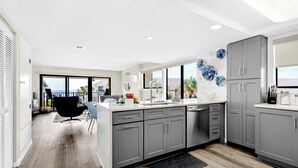 A modern kitchen with grey cabinets, a white countertop, and a view of the ocean through large windows.