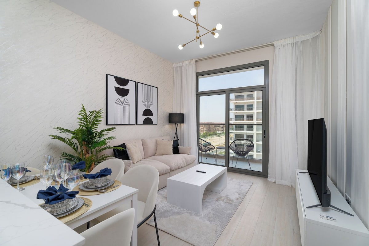 A modern living room with a sofa, coffee table, and dining area with glasses and plates. There is a TV and a plant.