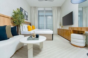 A modern hotel room with a bed, a sofa, a coffee table, a TV, and a plant. - Nasma Holiday Homes - Laya Heights (Dubai)