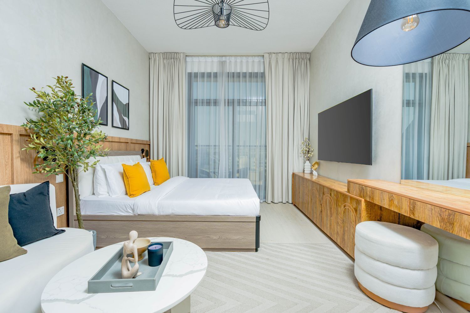 Een moderne hotelkamer met een bed, een bureau, een stoel, een televisie en een groot raam met gordijnen.