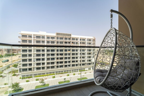Een balkon met een hangstoel, uitzicht op een meerhoog gebouw en een heldere lucht.
