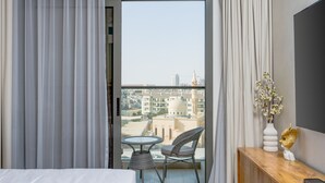 Ein Hotelzimmer mit Balkon, einem Bett, einem kleinen Tisch mit Stuhl und einer dekorativen Vase.