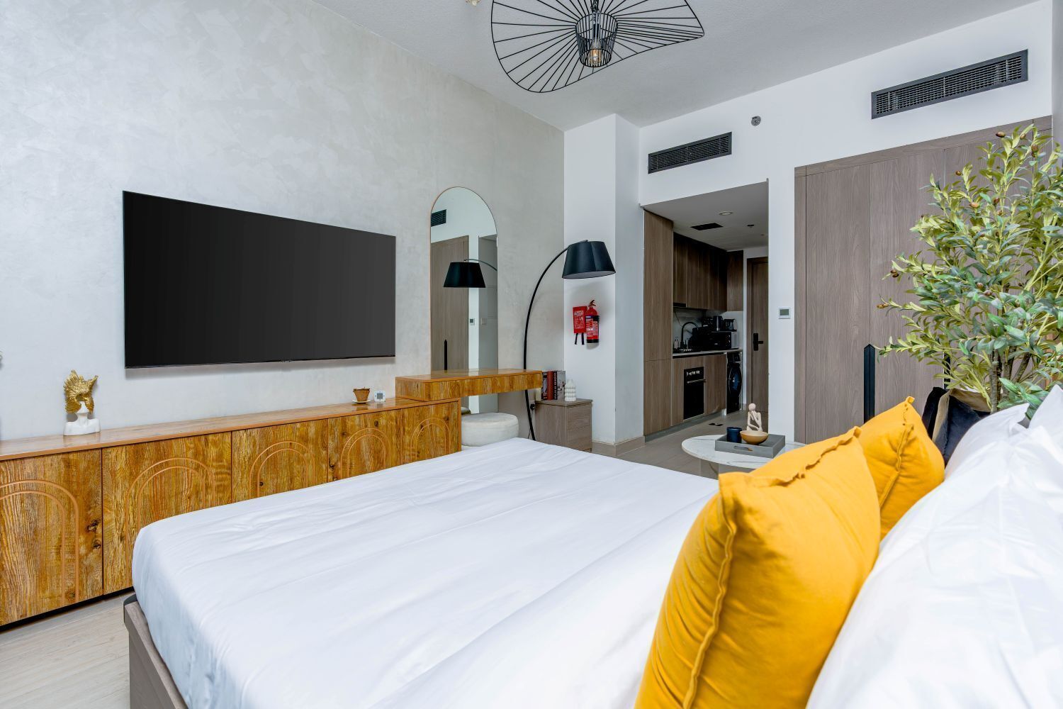 Una habitación de hotel moderna con una cama grande, una consola de madera, un televisor de pantalla plana, un espejo, una mesa redonda y una planta en maceta.