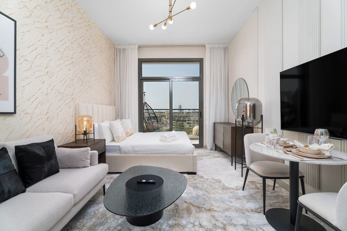 A modern hotel room with a bed, sofa, dining table, and a TV.