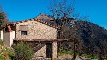Un bâtiment en pierre avec un toit en pente, une clôture en bois et une montagne en arrière-plan.
