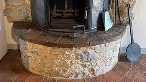 Una chimenea de piedra con parte superior y puerta de metal, rodeada de paredes de piedra y un piso de ladrillo.