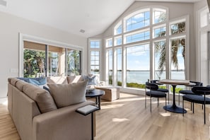 A spacious living area with a large window overlooking a body of water, a sofa, a small table, and a seating arrangement.