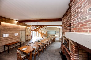 A spacious dining area with a long wooden table set for a meal, a brick fireplace, and a staircase leading to an upper level.