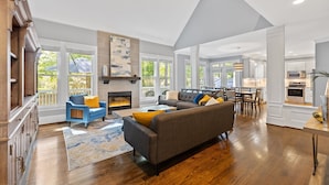 A spacious living area with a fireplace, a large sofa, and a dining area. - Spacious 5 Bedroom, Hot Tub, Arcade Room, EV Charger, Handicap & Quiet Culdesac! (Raleigh)