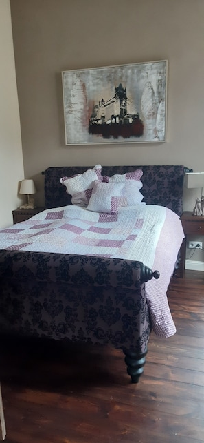A neatly made bed with a patterned bedspread, a headboard with a floral design, and a painting above the bed.