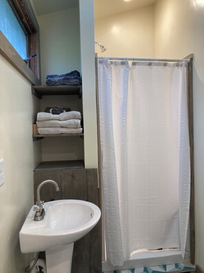 A bathroom with a white sink, a shower curtain, and shelves with folded towels. - A Cottage Minutes From Mad River Glen and Sugarbush  (Huntington)