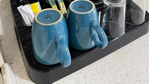 Una bandeja de cocina con cafetera, dos tazas azules, salero y pimentero, y sobres de azúcar y leche condensada.