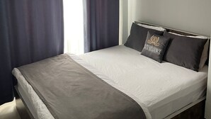 Un dormitorio con cama, cortinas oscuras, un ventanal blanco y una lámpara colgante.