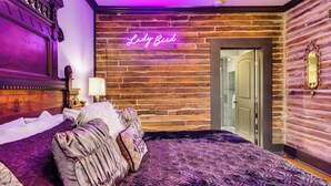 Een slaapkamer met een groot bed, een neonbord waarop 'Lady Bird' staat en een houten wand.