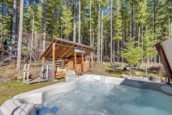 Un jacuzzi en un área boscosa, con una cabaña de madera al fondo.