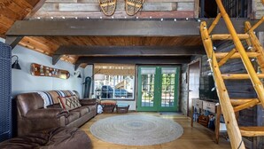 A cozy living room with a brown leather sofa, a round rug, and a wooden ladder. - Cabin at the Forest Edge | Hot tub, pet friendly (Packwood)