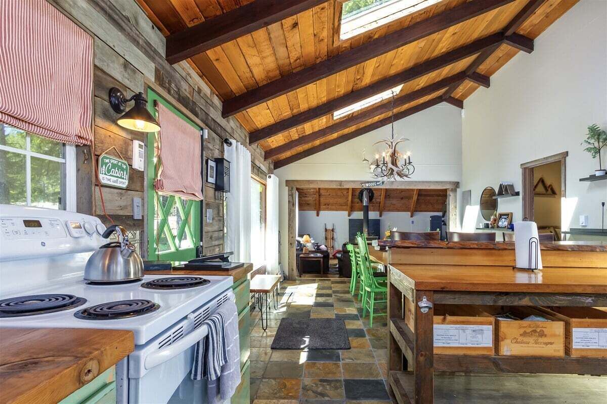 A rustic kitchen with a wooden ceiling, a stove, and a dining area with green chairs.
