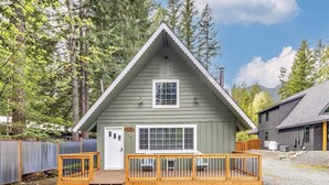 A small, single-story cabin with a wooden deck and a fenced yard. - Hygee Haus | Hot Tub, Wifi, Wood stove (Packwood)