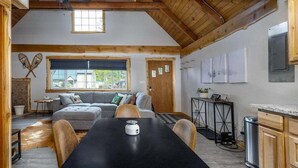 A cozy room with a wooden ceiling, a sofa, a dining table, and a kitchen area. - Hygee Haus | Hot Tub, Wifi, Wood stove (Packwood)