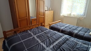 Une chambre avec deux lits, une armoire en bois, une commode et une fenêtre ornée de rideaux légers.