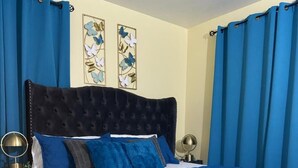 Een slaapkamer met een gestapeld hoofdbord, een bed met blauw beddengoed, twee wandlampen en een zacht, wit vloerkleed.