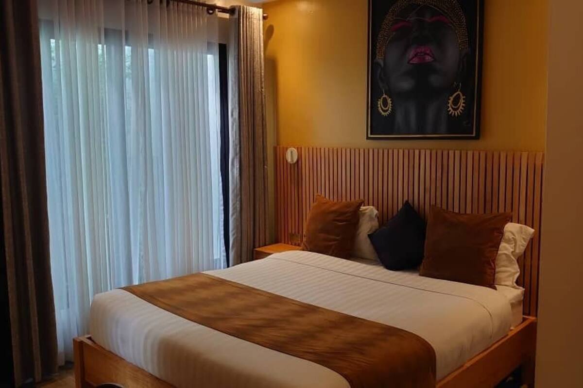 Une chambre d’hôtel avec un lit, des rideaux, une tête de lit et une œuvre d’art accrochée au mur.