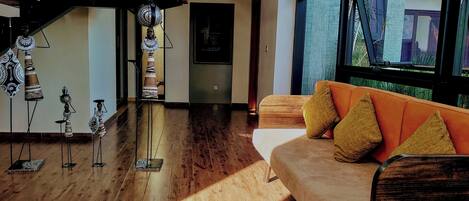 A modern living room with a wooden floor, a sofa with mustard pillows, and a staircase with decorative items.