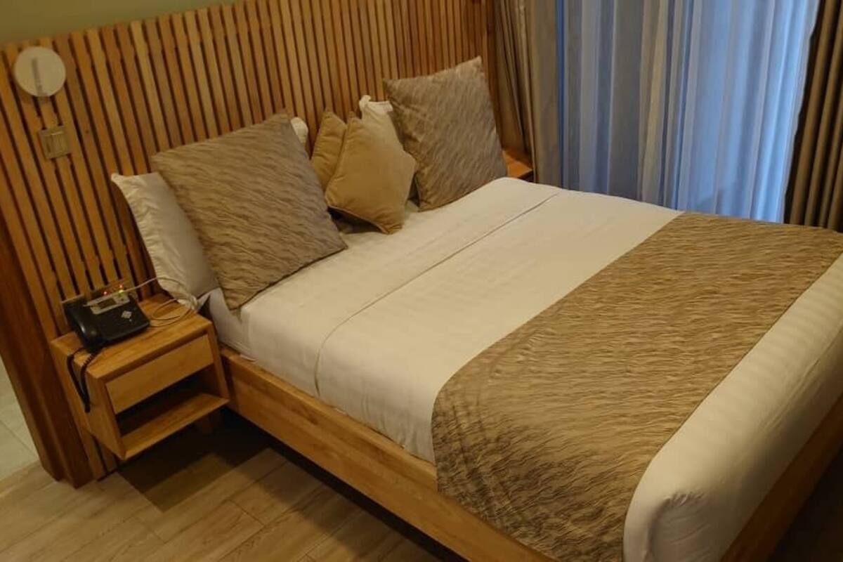 Un lit bien fait, avec une tête de lit en bois, une table de chevet avec une lampe et une prise électrique.
