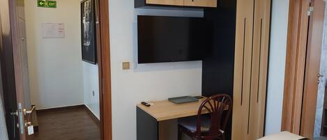 A bedroom with a bed, a desk, a chair, and a TV.