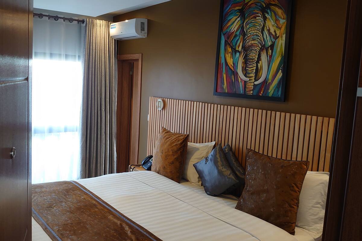 Une chambre d’hôtel avec un lit, un tableau, un appareil de climatisation et une vue sur l’extérieur.