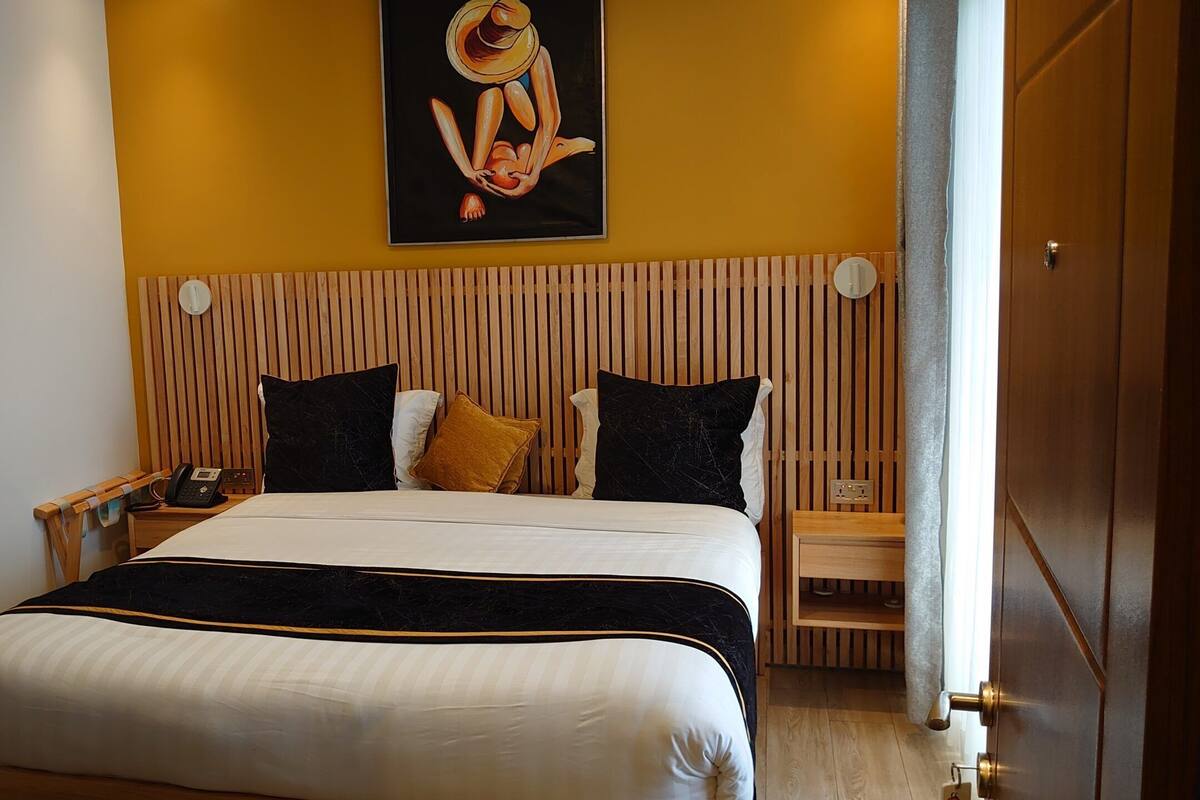 Une chambre d’hôtel avec un lit, une table de chevet avec un téléphone, un tableau accroché au mur et une tête de lit en bois.