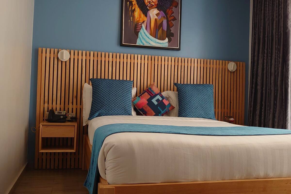 Un lit avec une tête de lit en bois, une couverture bleue et des coussins à motifs.