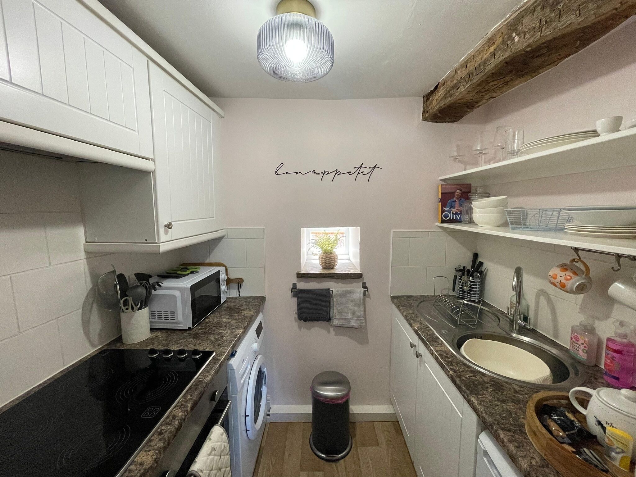 A compact kitchen with white cabinets, a microwave, a stove, a sink, and a small window.