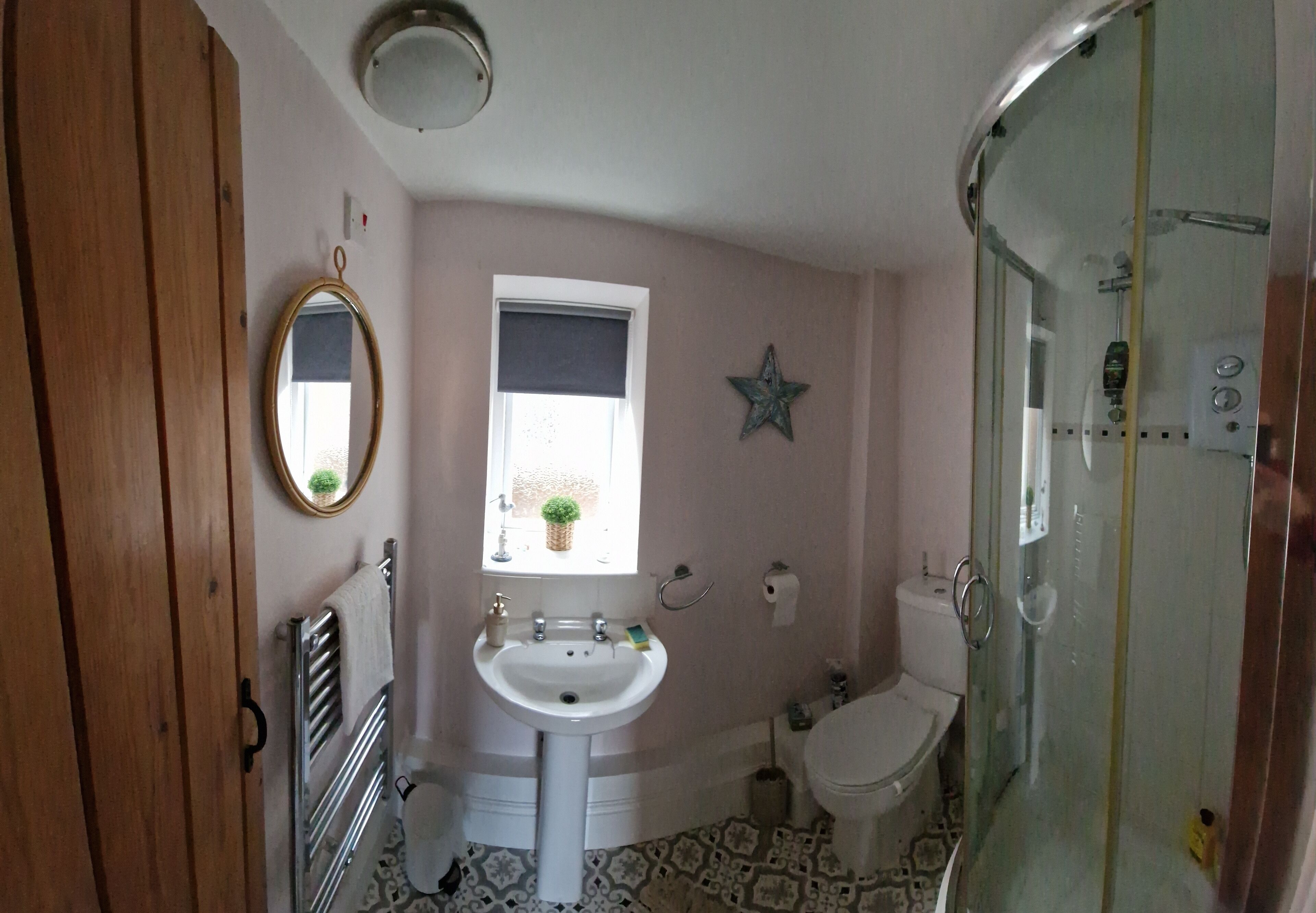 Un baño con lavamanos blanco, inodoro, cabina de ducha con mampara de vidrio, armario de madera, espejo y un adorno con forma de estrella en la pared.