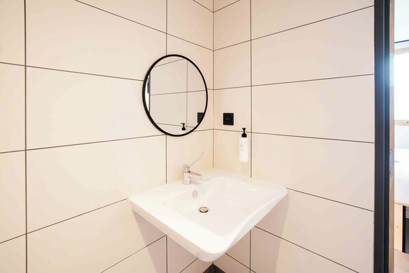 Un baño con un lavamanos blanco, un espejo redondo y un dispensador de jabón en la pared.