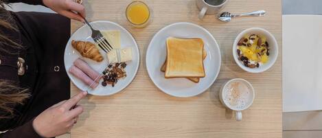 Una mesa de desayuno con croissant, queso, tostadas, fruta, café y jugo de naranja.