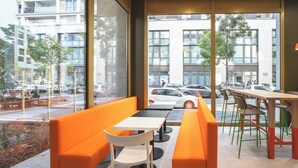A modern cafe with orange seating, large windows, and a view of the street. - easyHotel Marseille Euromed (Marseille)