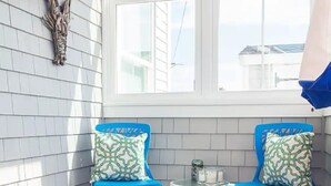 Un porche iluminado por el sol con dos sillas azules, una mesita y una lámpara de pared decorativa.