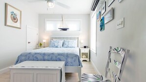 Un dormitorio con cama, mesitas de noche, un ventilador de techo y una ventana decorada con un velero.