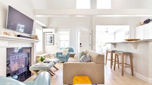 Amplia sala de estar con chimenea, televisor y una zona de cocina con taburetes.